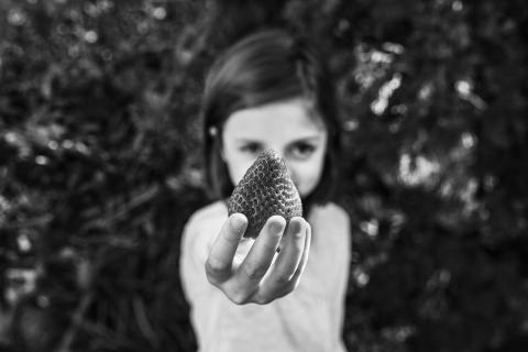 Black and white image of young girl holding out a strawberry