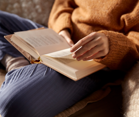 An open book on someone's lap with reader turning the page